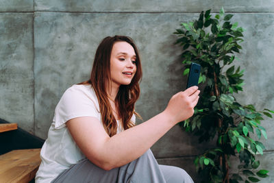 Young woman sitting on potted plant against wall