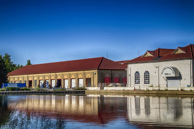 Buildings by lake against clear blue sky