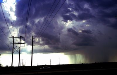Low angle view of electricity pylon against cloudy sky