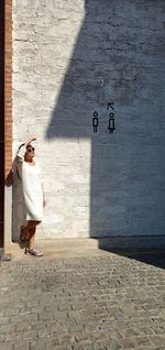 Woman standing on footpath against wall during sunny day