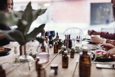 Multi-ethnic female colleagues eating lunch while sitting with various perfume bottles at table in workshop