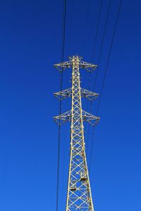 Low angle view of electricity pylon against clear blue sky