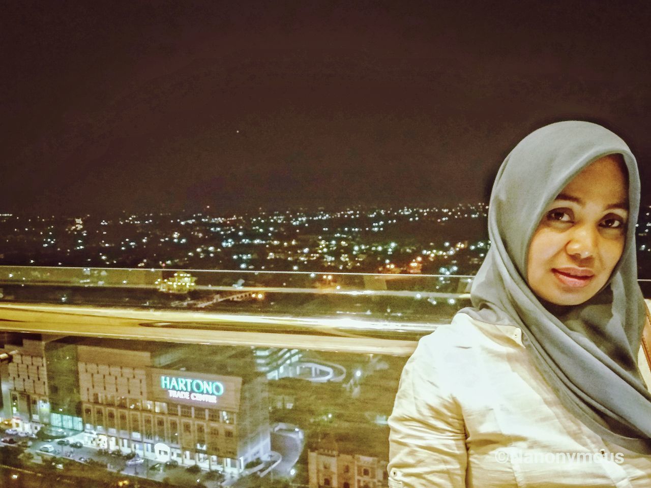 PORTRAIT OF YOUNG WOMAN WITH ILLUMINATED CITYSCAPE IN BACKGROUND