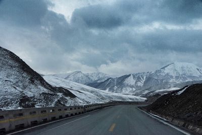 Road passing through snow covered mountains against cloudy sky
