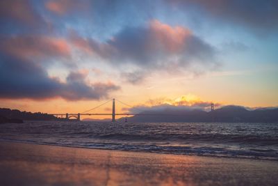 Suspension bridge over sea against sky during sunset