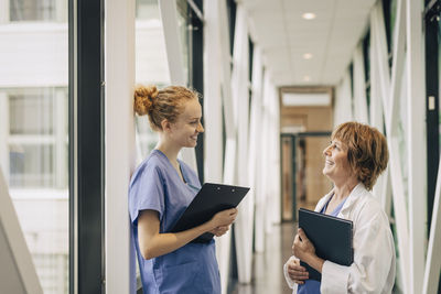 Side view of female healthcare workers discussing while standing in corridor