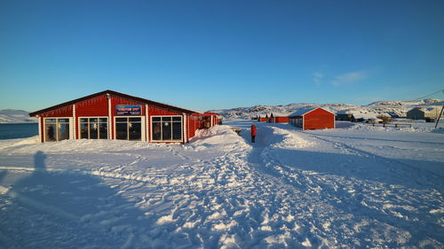Houses on snow covered land by building against blue sky