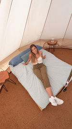 High angle view of smiling woman sitting on bed in tent