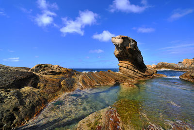 Rock formations by sea against blue sky