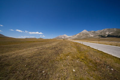 Street by field against blue sky