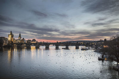 Bridge over river against buildings during sunset