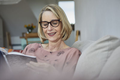 Smiling mature woman at home on the sofa reading a book
