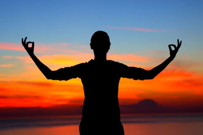 Silhouette woman with arms raised standing against sky during sunset