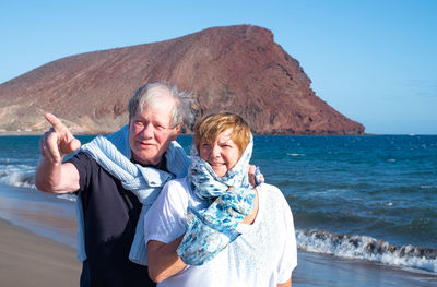 Senior man showing something to woman standing at beach