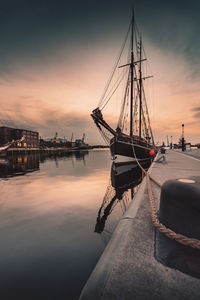 Sailboats moored in sea against sky during sunset