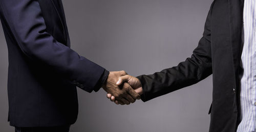 Midsection of businessmen shaking hands on gray background