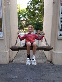 Full length portrait of smiling girl sitting on swing outdoors