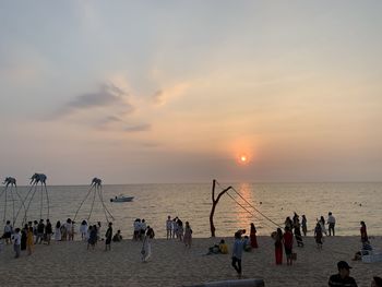 Group of people on beach against sky during sunset