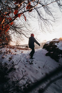 Full length of man standing on snow covered tree during sunset