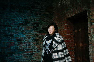 Portrait of woman standing against brick wall