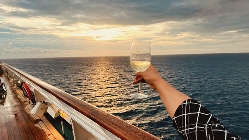 Cropped hand of woman holding drink in sea against sky