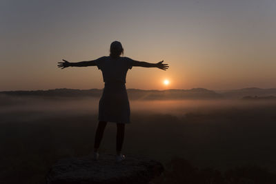 Silhouette of girl at the top of a mountain at sunrise with arms out