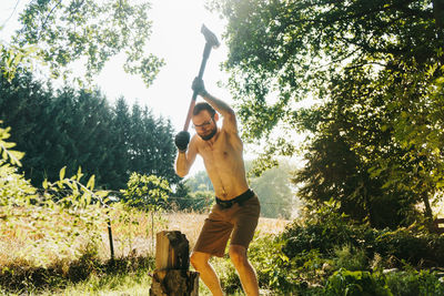 Shirtless lumberjack cutting wood on field