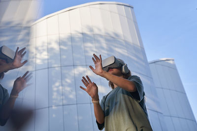 Teenage girl in vr helmet in the park on background of modern building 