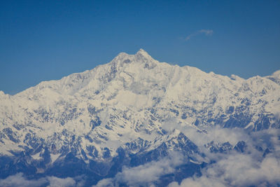 Low angle view of snowcapped mountains against clear blue sky