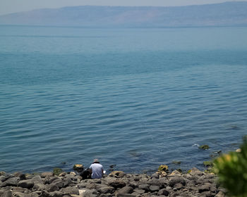 Rear view of men sitting on rock by sea