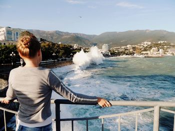 Man standing on railing by sea against sky