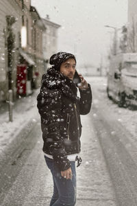 Man talking on phone while standing on street in city during winter