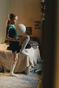 Female athlete playing with soccer ball standing in bedroom at home