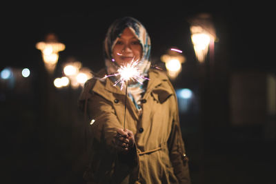 Young woman with burning sparkler at night
