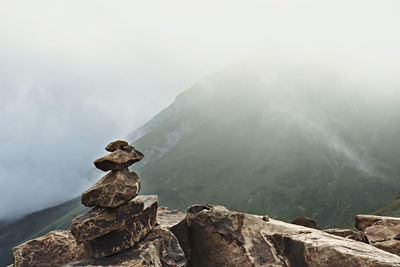 View of tower or pyramid of stones in rocky mountains in clouds ridge in fog hike natural background