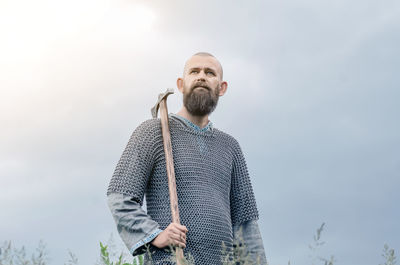 Viking. a bald bearded man in metal chain mail over linen shirt holds ax.