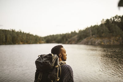 Rear view of man with backpack looking away against lake in forest