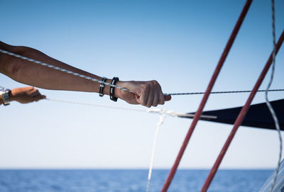 Cropped hand of man holding rope in sailboat against sky