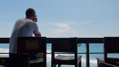 Rear view of man sitting on chair at boat deck