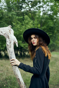 Portrait of young woman wearing hat standing against trees