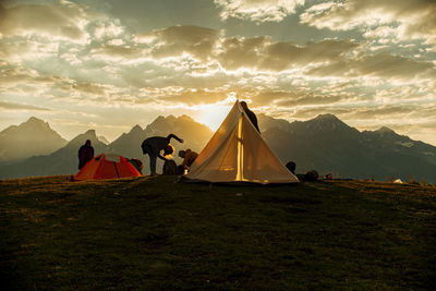 Friends camping on mountain against cloudy sky