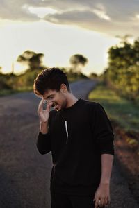 Smiling young man standing on road during sunset