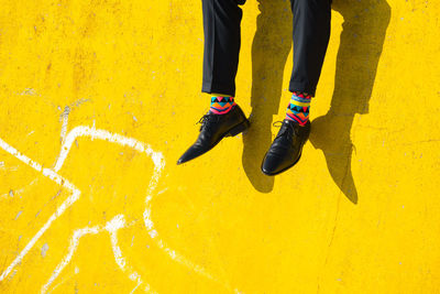 Low section of man wearing shoes while sitting on yellow wall
