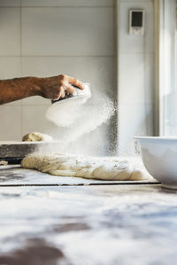 Cropped hand sifting flour on dough in kitchen