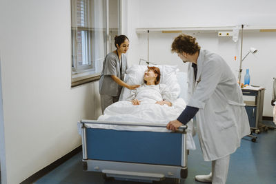 Smiling female senior patient lying on bed amidst healthcare workers at hospital