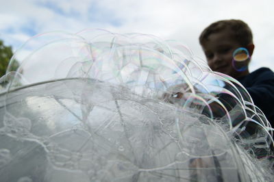 Boy standing by bubbles on umbrella against sky