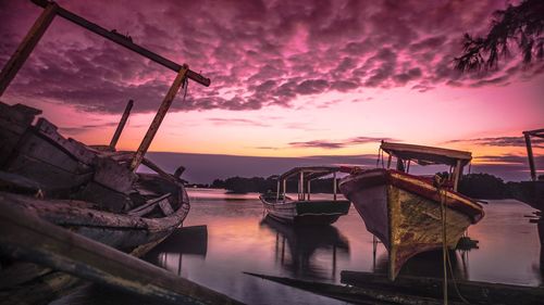 Boats moored in sea against dramatic sky during sunset
