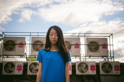 Young woman with eyes closed standing against exhaust fans