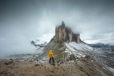 Rear view of hiker standing on rock against sky