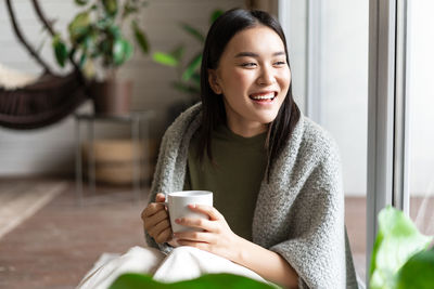 Portrait of young woman using mobile phone while sitting at home